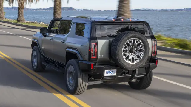 2024 GMC HUMMER EV SUV drives down a coastal road with palm trees.