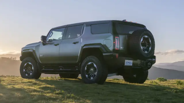 Rear 3/4 view of 2024 GMC HUMMER EV SUV in Moonshot Green Matte overlooking an off-road sunset.