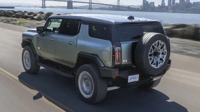 2024 GMC HUMMER EV SUV driving on coastal road with San Francisco skyline and Bay Bridge in the background.