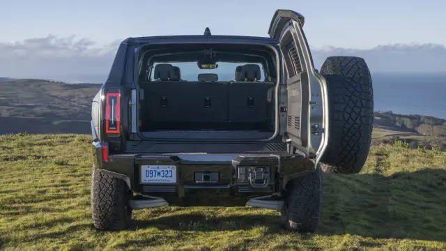 Rear shot of 2024 GMC HUMMER EV SUV with open swing-gate in grassy off-road location. With the rear seats folded down, the HUMMER EV SUV features 81.8 cubic feet of cargo space.
