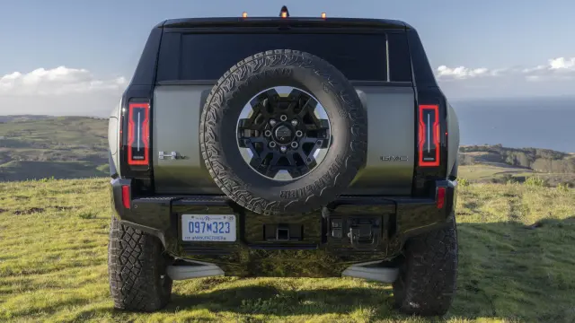 Rear shot of 2024 GMC HUMMER EV SUV parked off-road highlighting the closed swing-gate and standard full-size spare tire mounted to the back of the vehicle.