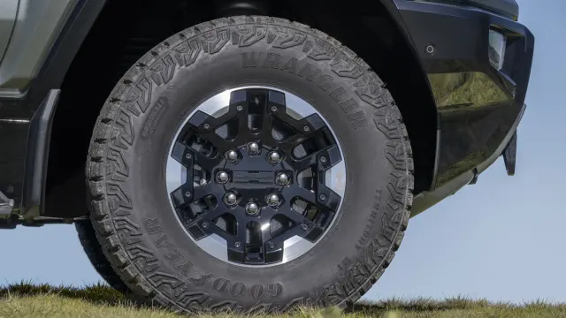 Close-up of front passenger wheel of 2024 GMC HUMMER EV SUV with 18-inch black aluminum wheels with machined accents and Goodyear Wrangler Territory Mud Terrain tires.