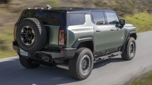 Rear 3/4 shot of 2024 GMC HUMMER EV SUV driving on rural road.