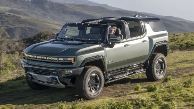 Front 3/4 shot of the 2024 GMC HUMMER EV SUV with Sky Panels removed descending an off-road course against a mountainous backdrop.
