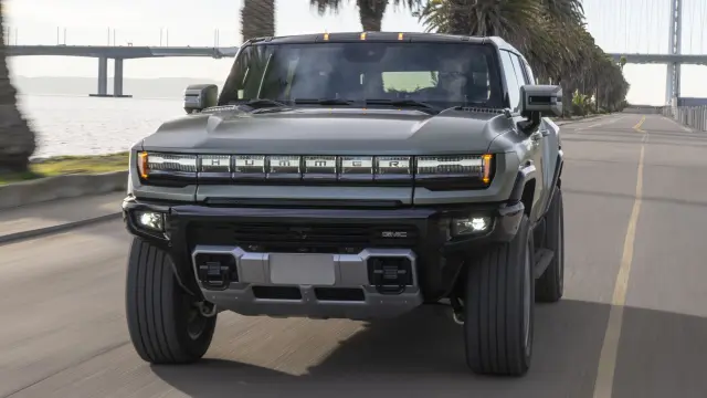 2024 GMC HUMMER EV SUV in Moonshot Green Matte driving on two lane coastal road with palm trees and bridge in the background.